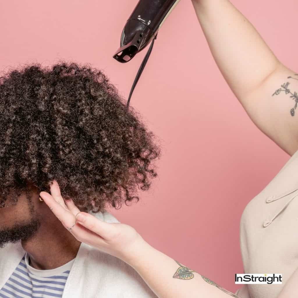lady blow drying the hair of a man with an afro hair