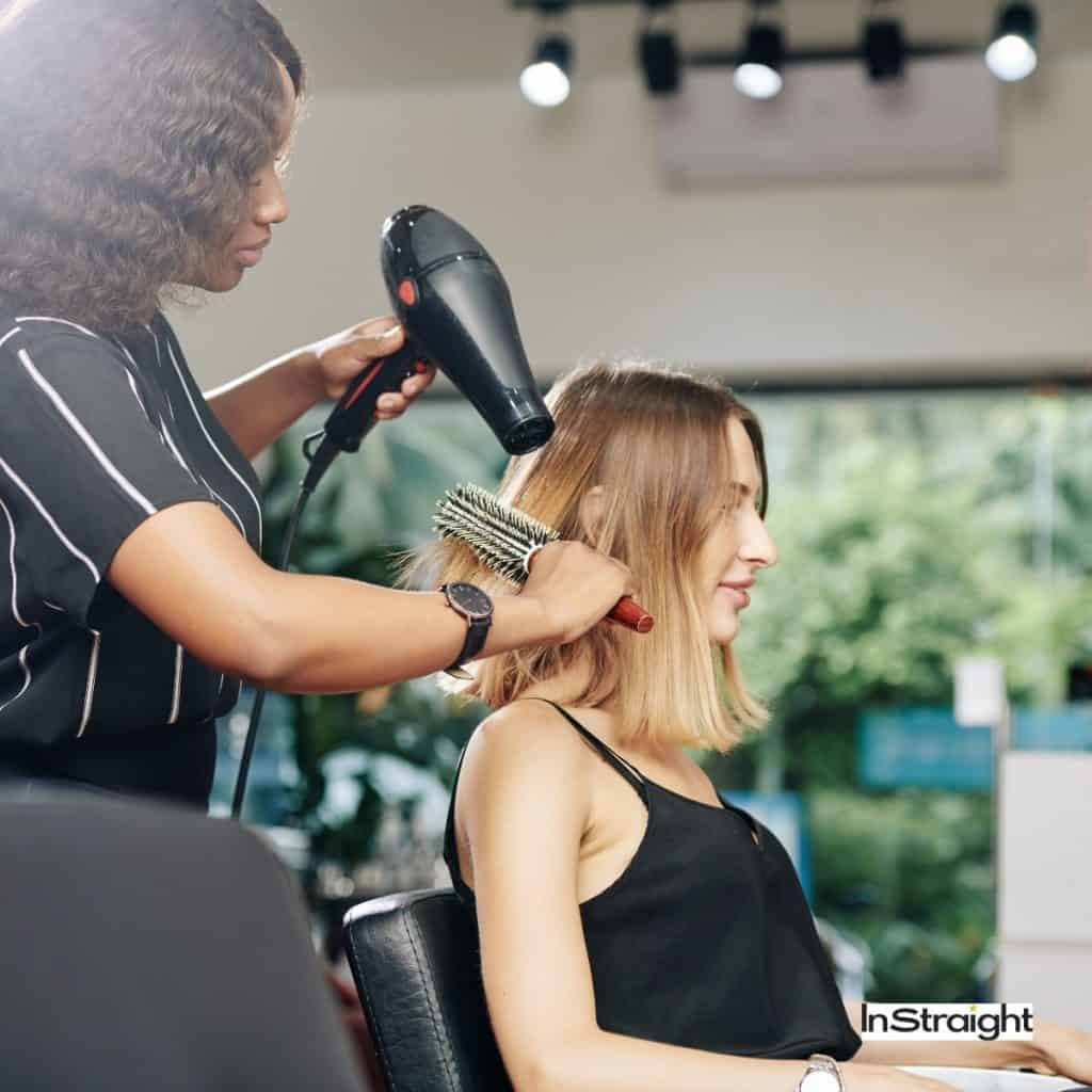Lady with medium length hair getting a blow dry in a salon under the title How To Blowout Medium-Length Hair Like A Pro