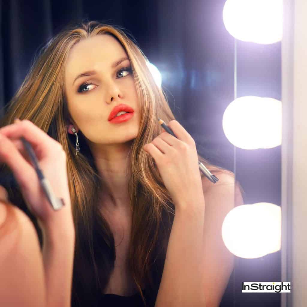 A lady applying makeup infront of a lit mirror  under title Are Backlit Mirrors Good for Makeup?